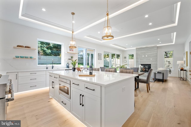 kitchen with white cabinetry, a raised ceiling, pendant lighting, a tiled fireplace, and a kitchen island