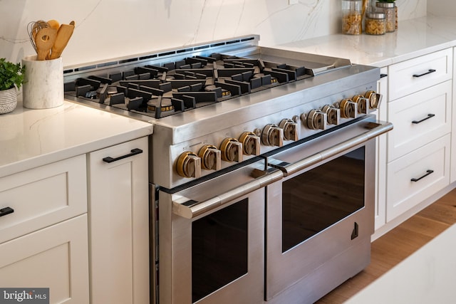 room details featuring tasteful backsplash, white cabinetry, double oven range, and light hardwood / wood-style floors