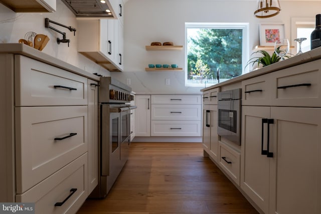 kitchen featuring backsplash, light wood-type flooring, decorative light fixtures, stainless steel range oven, and white cabinetry