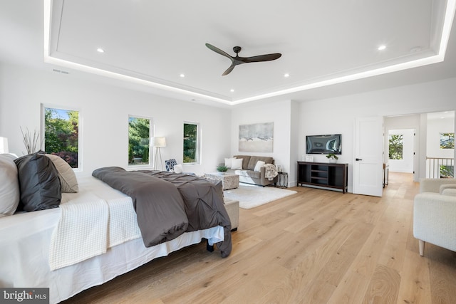 bedroom featuring a raised ceiling, ceiling fan, and light wood-type flooring