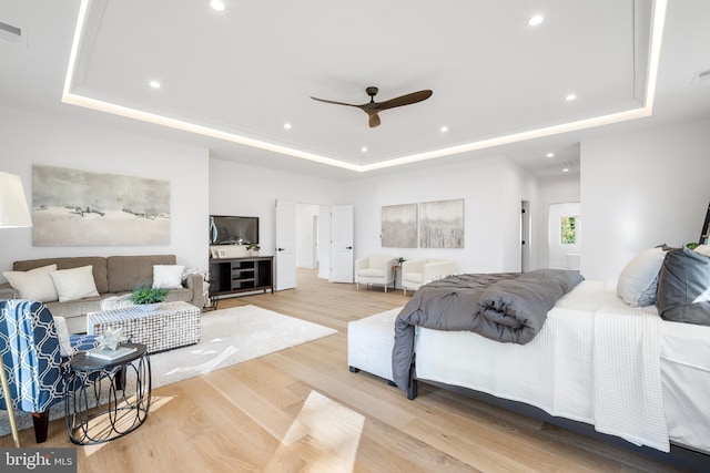 bedroom with a raised ceiling, ceiling fan, and light hardwood / wood-style flooring