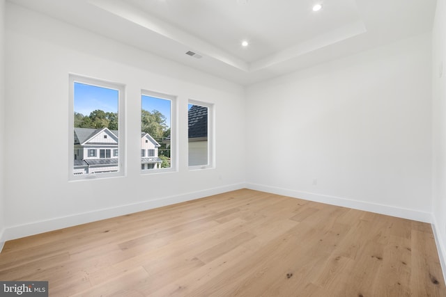 spare room with a tray ceiling and light hardwood / wood-style flooring