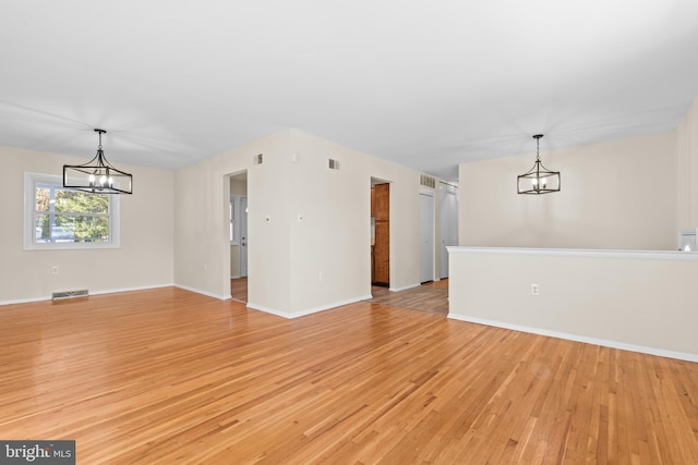 spare room featuring a chandelier and light wood-type flooring