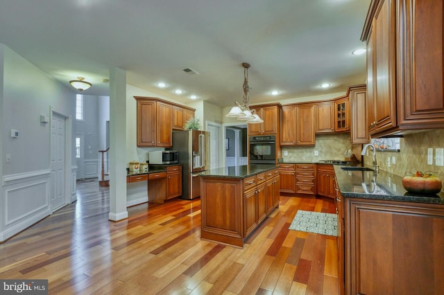 kitchen featuring sink, hanging light fixtures, stainless steel appliances, dark stone countertops, and a kitchen island