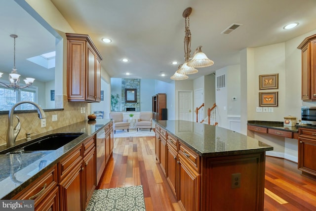 kitchen featuring wood-type flooring, hanging light fixtures, dark stone countertops, and sink