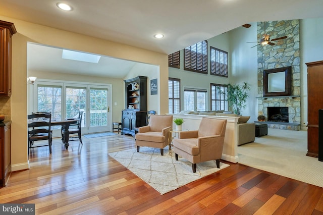 living room with ceiling fan, a stone fireplace, a wealth of natural light, and a skylight