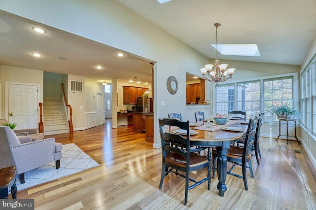 dining space with lofted ceiling with skylight, a chandelier, and light wood-type flooring