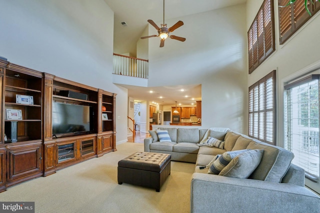 carpeted living room with ceiling fan and a high ceiling