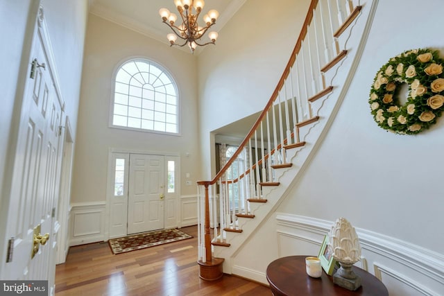 foyer entrance with a towering ceiling, light hardwood / wood-style flooring, an inviting chandelier, and crown molding