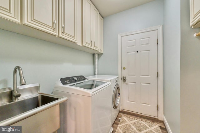 clothes washing area featuring cabinets, washing machine and dryer, light hardwood / wood-style floors, and sink