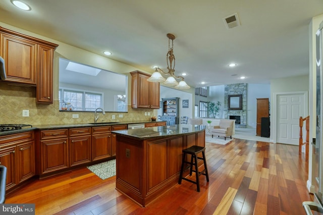 kitchen with sink, hanging light fixtures, a kitchen bar, a fireplace, and a kitchen island