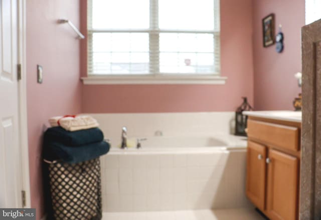 bathroom featuring tiled tub, vanity, and a healthy amount of sunlight