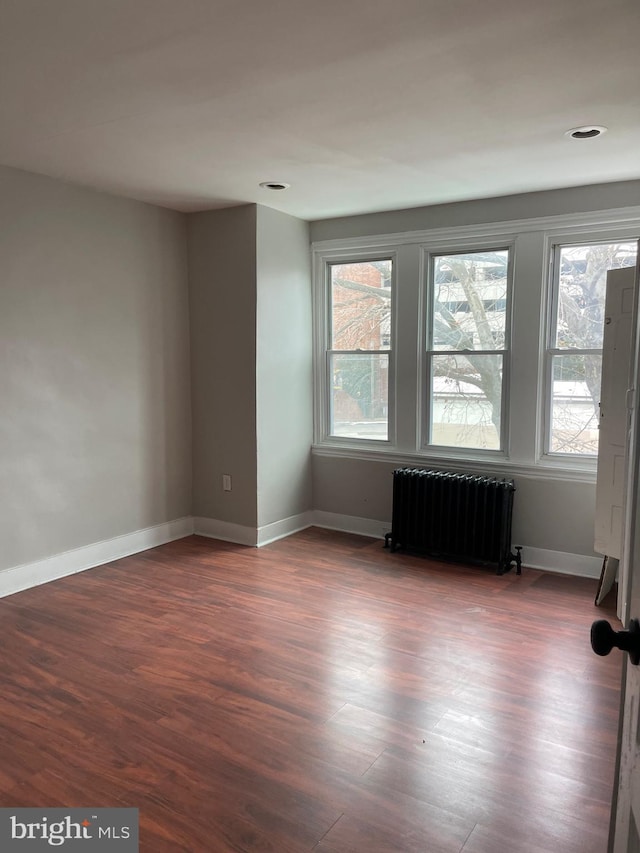 spare room with dark hardwood / wood-style flooring, plenty of natural light, and radiator