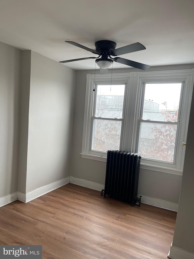 spare room with ceiling fan, radiator heating unit, a healthy amount of sunlight, and hardwood / wood-style flooring