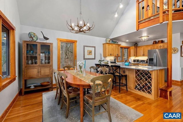 dining area featuring high vaulted ceiling, a chandelier, and light hardwood / wood-style floors