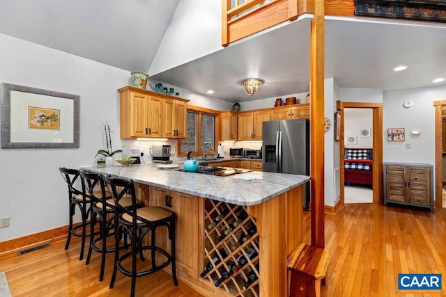 kitchen with kitchen peninsula, light stone countertops, light hardwood / wood-style floors, stainless steel fridge with ice dispenser, and a breakfast bar area