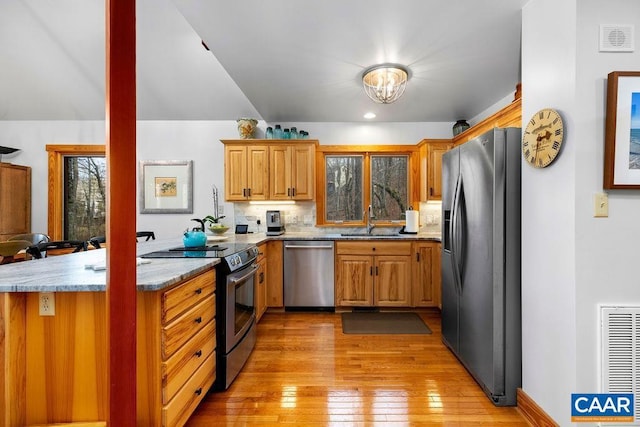 kitchen with kitchen peninsula, backsplash, stainless steel appliances, sink, and light hardwood / wood-style flooring