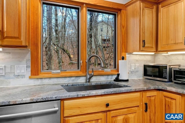 kitchen with appliances with stainless steel finishes, tasteful backsplash, light stone counters, and sink