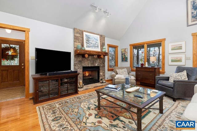 living room featuring light wood-type flooring, track lighting, high vaulted ceiling, and a stone fireplace