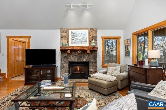 living room with hardwood / wood-style floors, a stone fireplace, and lofted ceiling