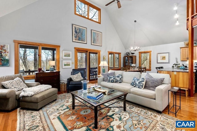 living room featuring ceiling fan with notable chandelier, light hardwood / wood-style flooring, and high vaulted ceiling