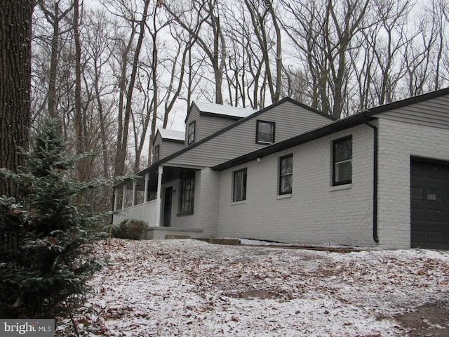 snow covered property featuring covered porch and a garage