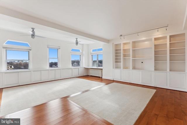 unfurnished living room featuring radiator, built in shelves, track lighting, and hardwood / wood-style flooring