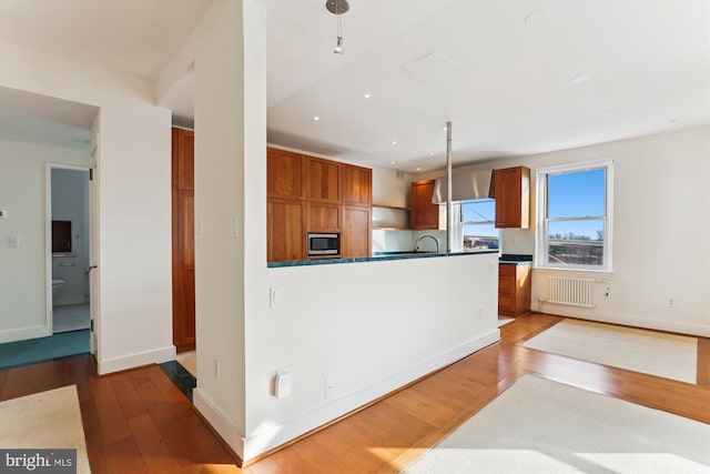 kitchen with hardwood / wood-style floors, decorative light fixtures, stainless steel microwave, and radiator heating unit