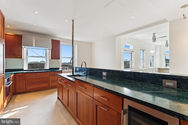 kitchen with stainless steel oven, dark stone counters, sink, ceiling fan, and beverage cooler