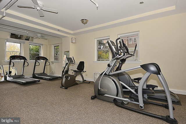 gym featuring a raised ceiling and ceiling fan