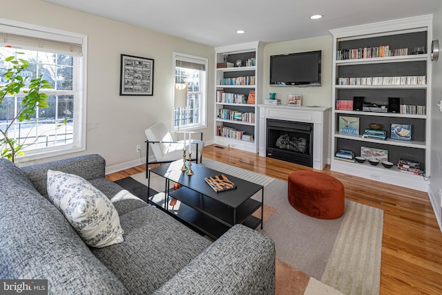 living room with built in shelves, plenty of natural light, and wood-type flooring