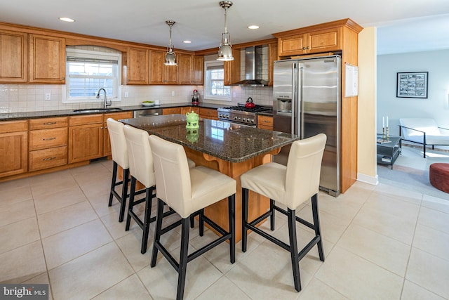 kitchen with sink, wall chimney exhaust hood, premium appliances, dark stone counters, and a kitchen island