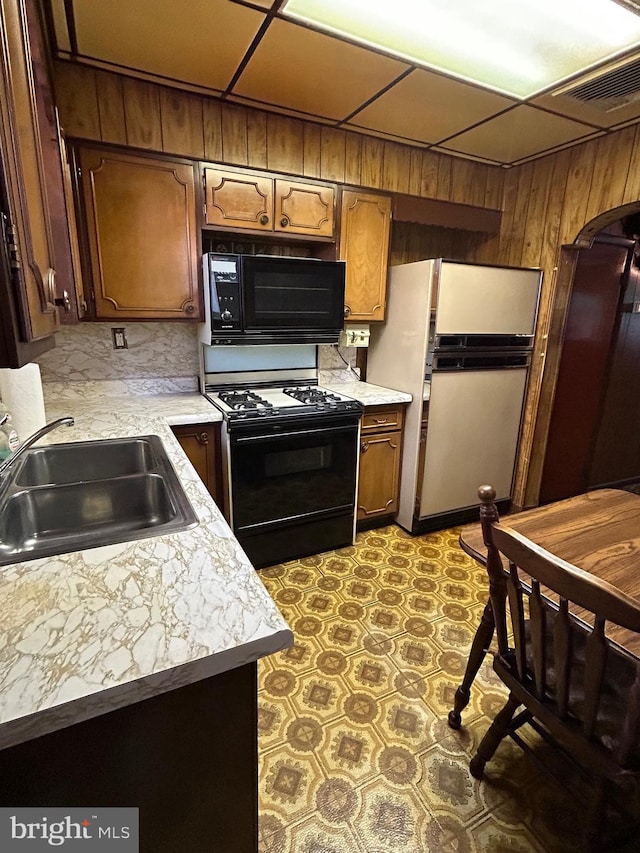 kitchen with sink, a paneled ceiling, wood walls, and black appliances