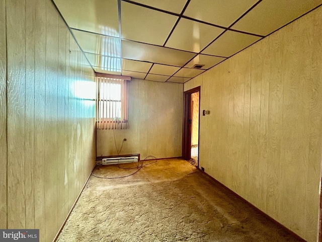 spare room with carpet flooring, wooden walls, a drop ceiling, and baseboard heating