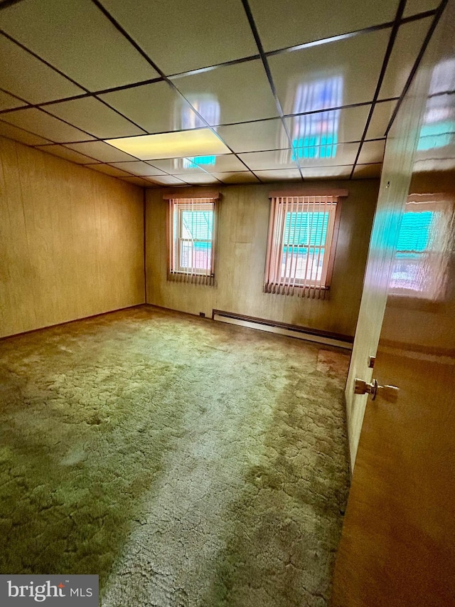 basement with a baseboard radiator, a drop ceiling, carpet, and wood walls