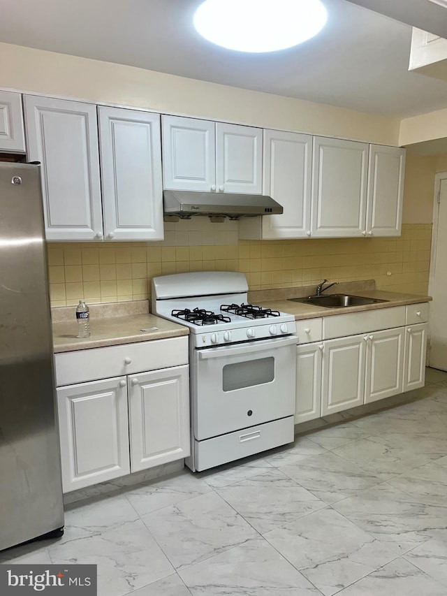 kitchen with backsplash, white cabinets, sink, white range with gas stovetop, and stainless steel refrigerator