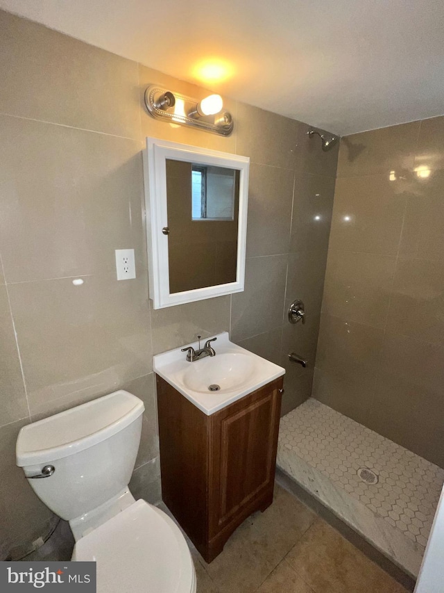 bathroom with vanity, tile patterned flooring, toilet, tiled shower, and tile walls