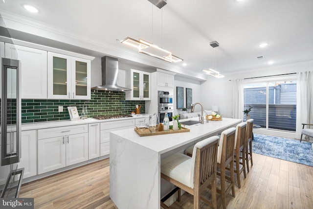 kitchen with white cabinets, sink, wall chimney exhaust hood, and pendant lighting