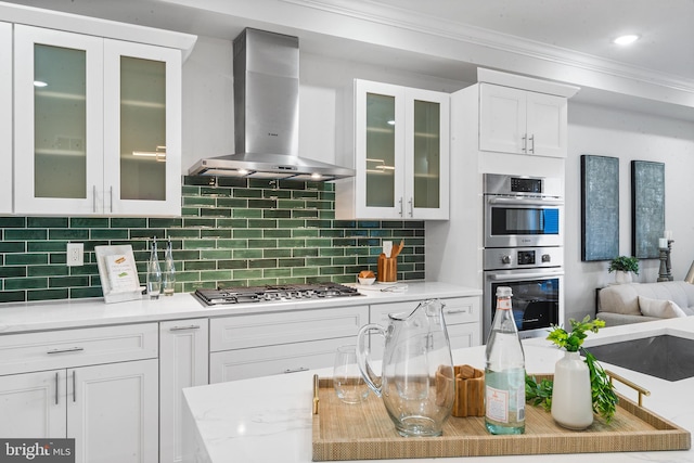 kitchen featuring decorative backsplash, ornamental molding, wall chimney exhaust hood, stainless steel appliances, and white cabinets