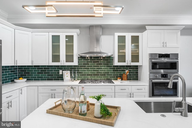 kitchen with white cabinets, wall chimney range hood, appliances with stainless steel finishes, and tasteful backsplash