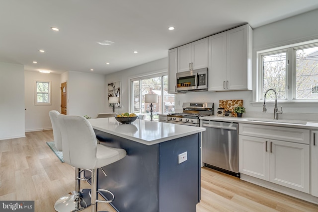 kitchen with appliances with stainless steel finishes, light wood-type flooring, a kitchen island, sink, and white cabinetry