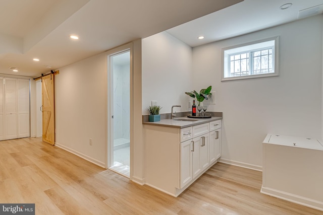 bar with light wood-type flooring, a barn door, white cabinetry, and sink