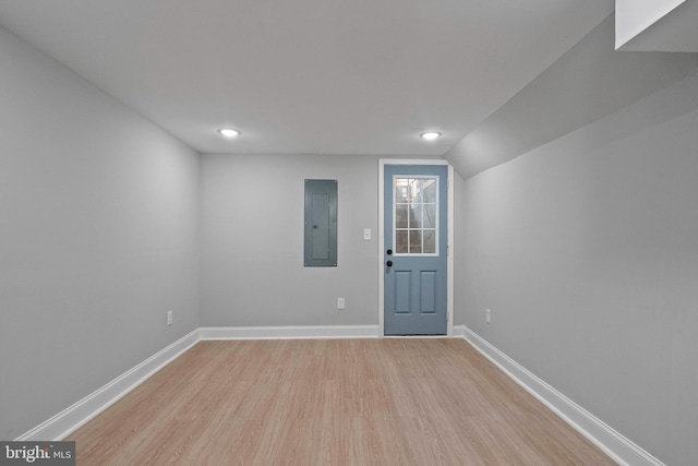 empty room featuring light wood-type flooring, electric panel, and lofted ceiling