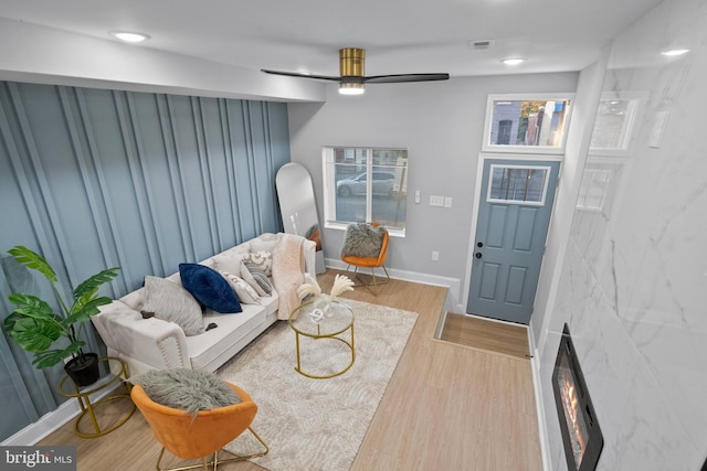 living room with ceiling fan, a large fireplace, and light wood-type flooring