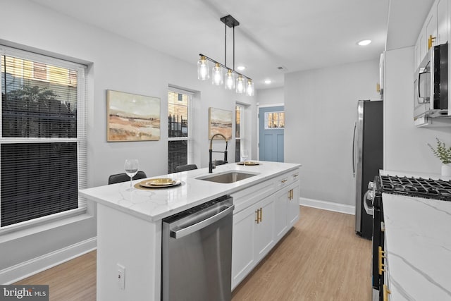 kitchen with light stone countertops, stainless steel appliances, sink, a center island with sink, and white cabinetry