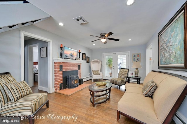 living room with ceiling fan, a baseboard heating unit, light wood-type flooring, a wood stove, and french doors