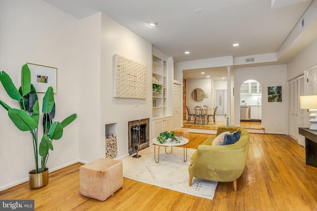 living room featuring built in shelves, decorative columns, and light hardwood / wood-style flooring