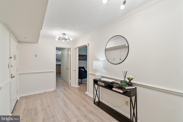 corridor with crown molding, light hardwood / wood-style floors, a textured ceiling, and an inviting chandelier