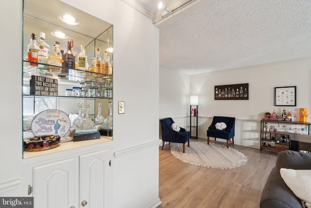 bar featuring a textured ceiling, light hardwood / wood-style flooring, and ornamental molding