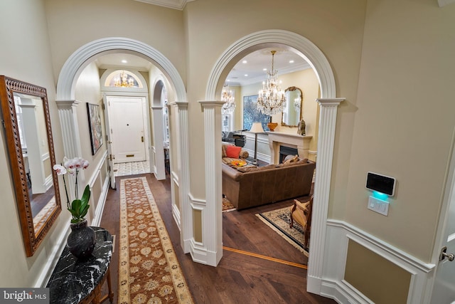 corridor with crown molding, dark wood finished floors, decorative columns, recessed lighting, and an inviting chandelier